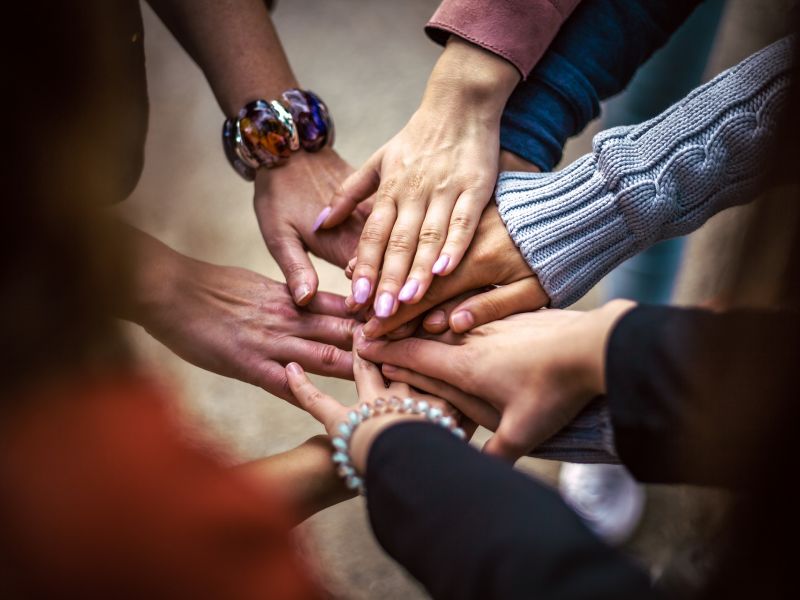 Na zdjęciu ręce ludzi złożone jedna na drugiej w geście współpracy i przyjaźni