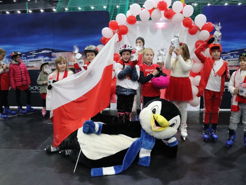 Na zdjęciu uczestnicy ślizgawki niepodległościowej w Arenie Lodowej/ Wszyscy w biało-czerwonych barwach pozują do zdjęcia razem z maskotką Areny - Pingwinem