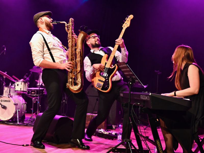 Na zdjęciu basista i saksofonista grupy Głowny Zawór Jazzu podczas występu na scenie MCK Tkacz. Obok przy pianinie gra pianistka