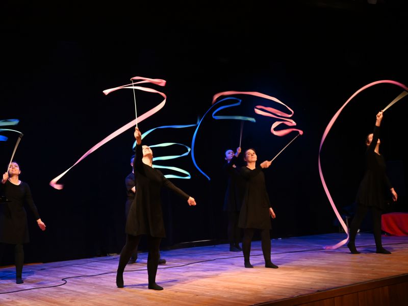 Na zdjęciu dziewczyny ubrane na czarno tańcż ze wstążkami na scenie