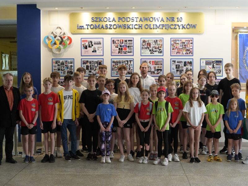 Na zdjęciu uczniowie SP nr 10 wraz z dyrektorem szkoły pozują na korytarzu szkolnym do fotografii z olimpijczykiem Damianemżurkiem